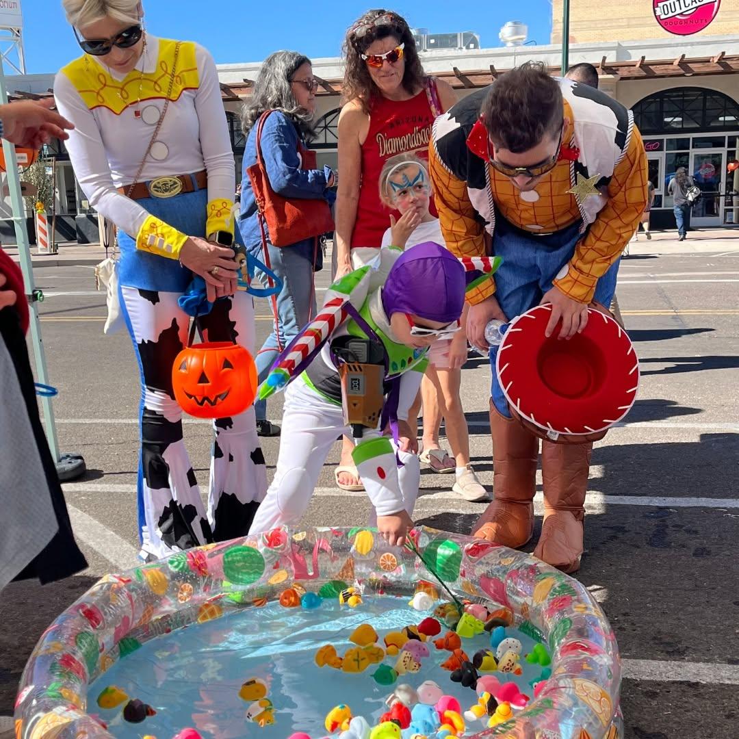 A child and adults dressed as Toy Story characters choose treats in Downtown Mesa.