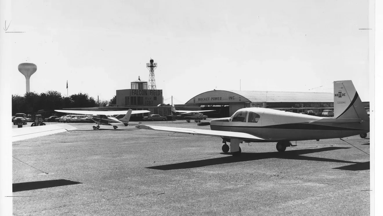 Black-and-white photograph of aircraft parked at Falcon Field with its control tower in the background.